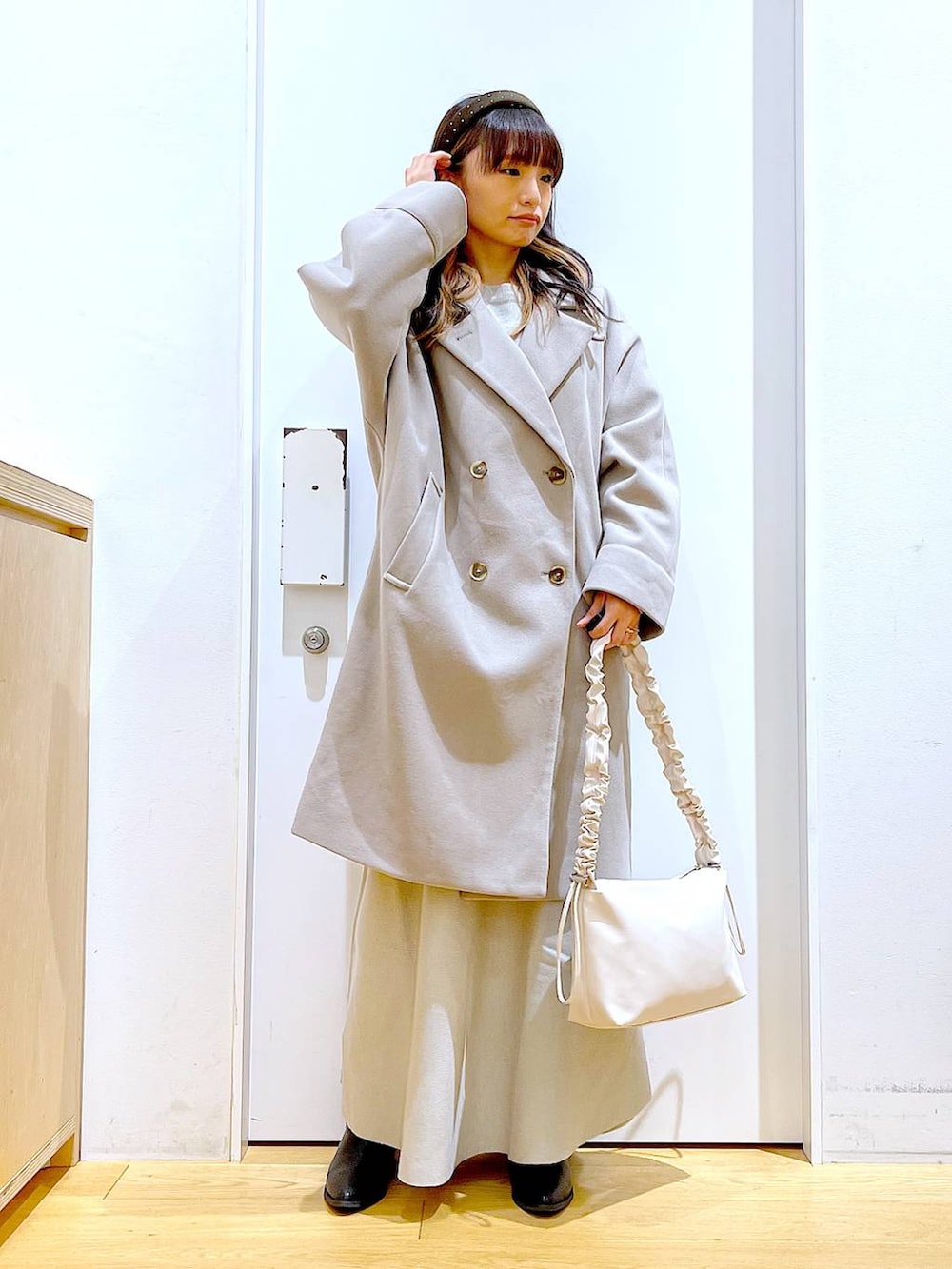 グレー系のステンカラーコート、ホワイト系のショルダーバッグ、グレー系のスカートを着用したレディースの冬コーディネートの2枚目の写真