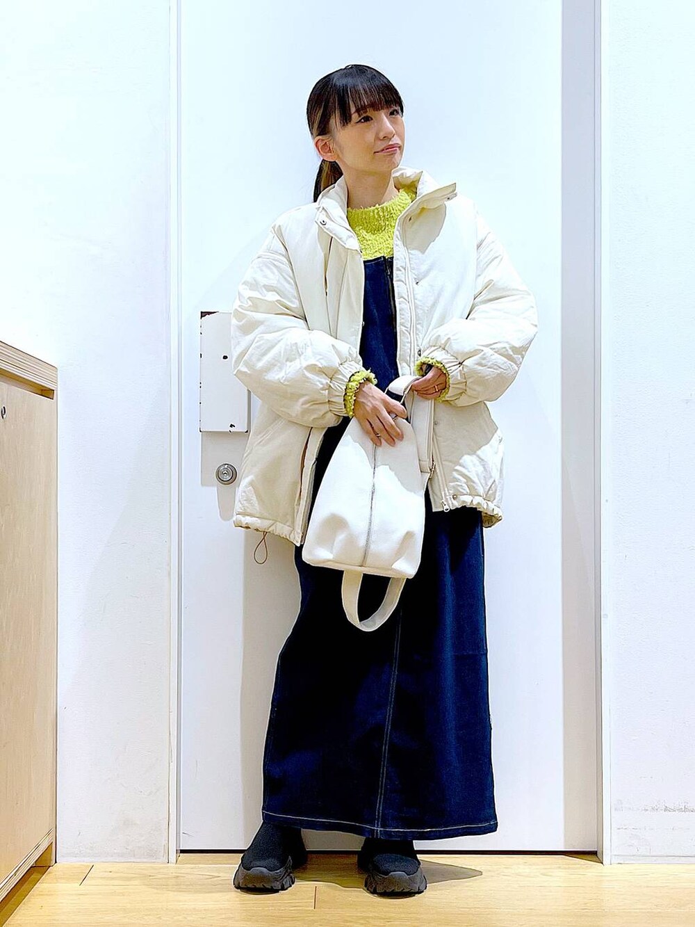 グリーン系のニット/セーター、ブルー系のジャンパースカート、ホワイト系のボディバッグ/ウエストポーチを着用したレディースの冬コーディネートの2枚目の写真