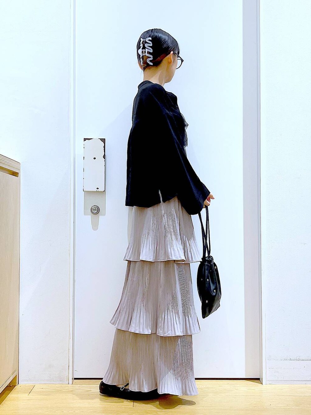 グレー系のスカート、ブラック系のショルダーバッグ、ブラック系のパンプスを着用したレディースの秋コーディネートの4枚目の写真