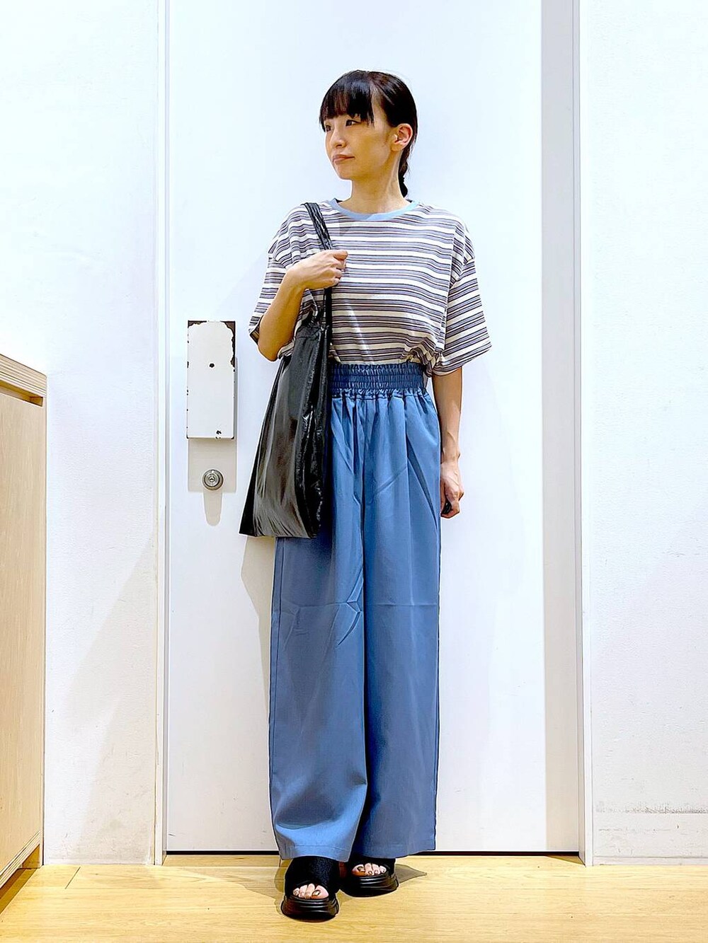 ブラック系のトートバッグ、ブラック系のサンダル、ベージュ系のTシャツ/カットソーを着用したレディースの夏コーディネートの2枚目の写真