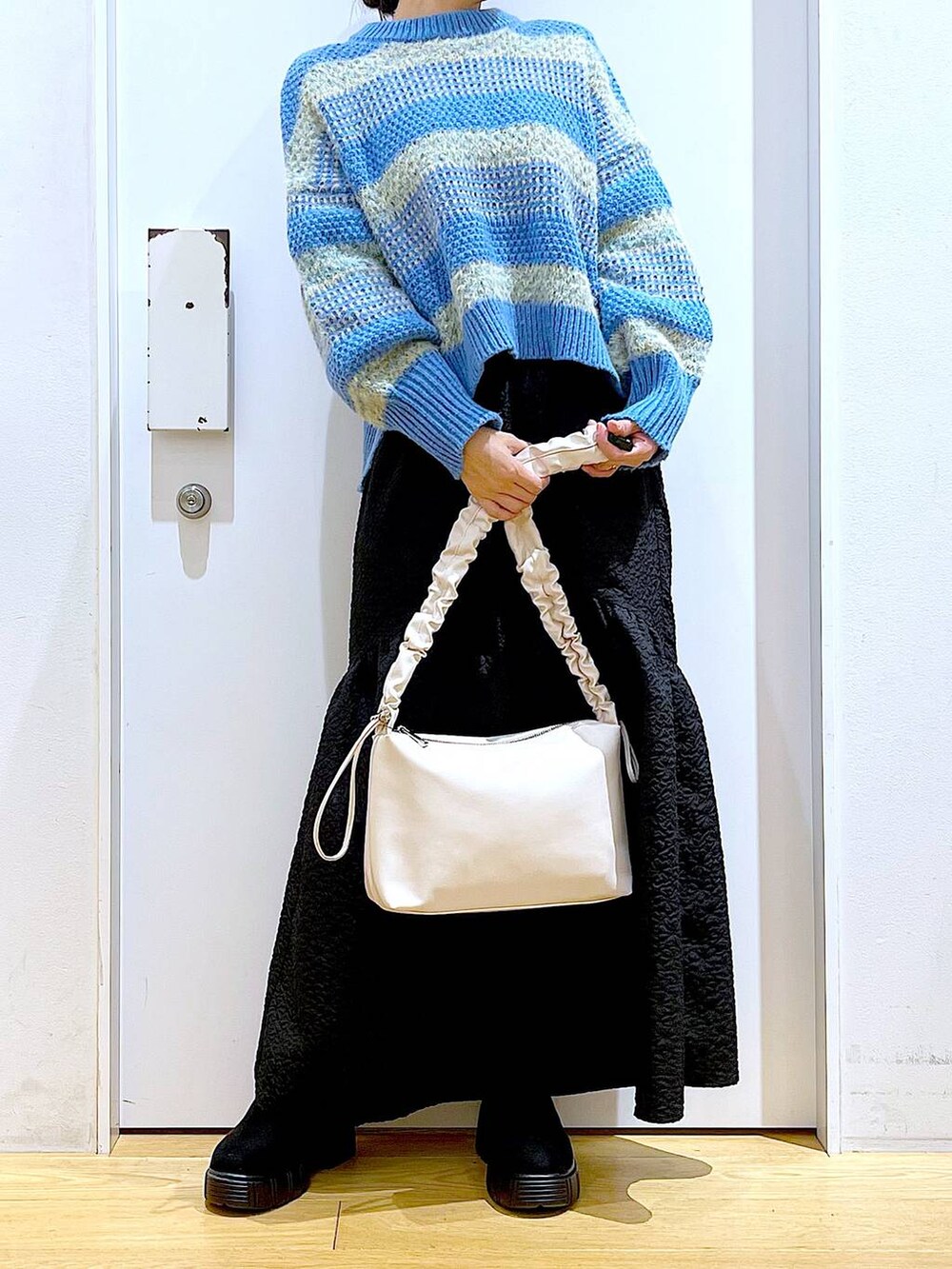 ホワイト系のショルダーバッグ、ブラック系のブーツ、ブラック系のスカートを着用したレディースの冬コーディネートの6枚目の写真