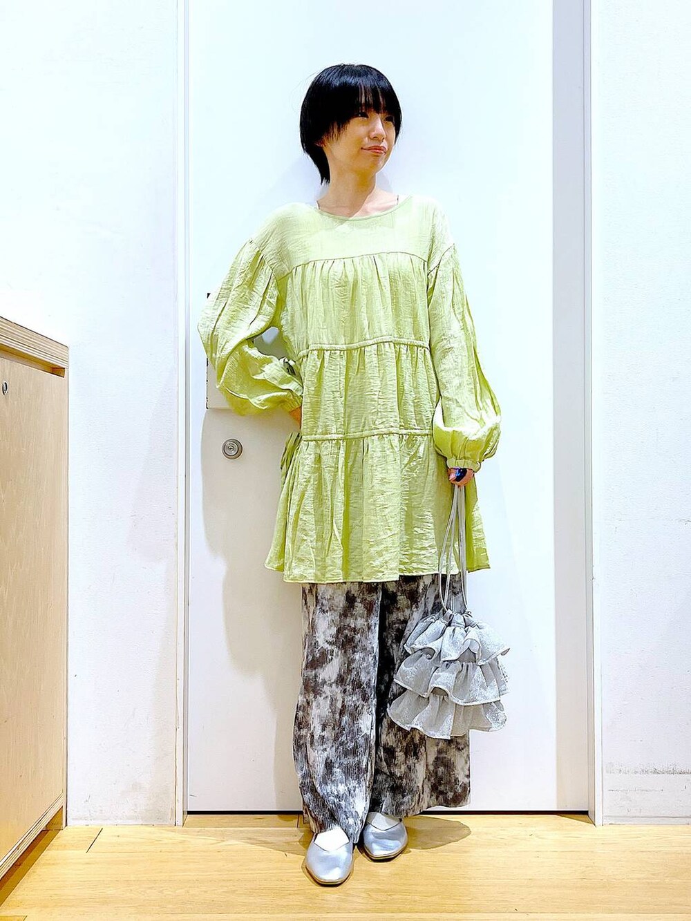 シルバー系のショルダーバッグ、シルバー系のパンプス、グリーン系のチュニックを着用したレディースの春コーディネートの2枚目の写真