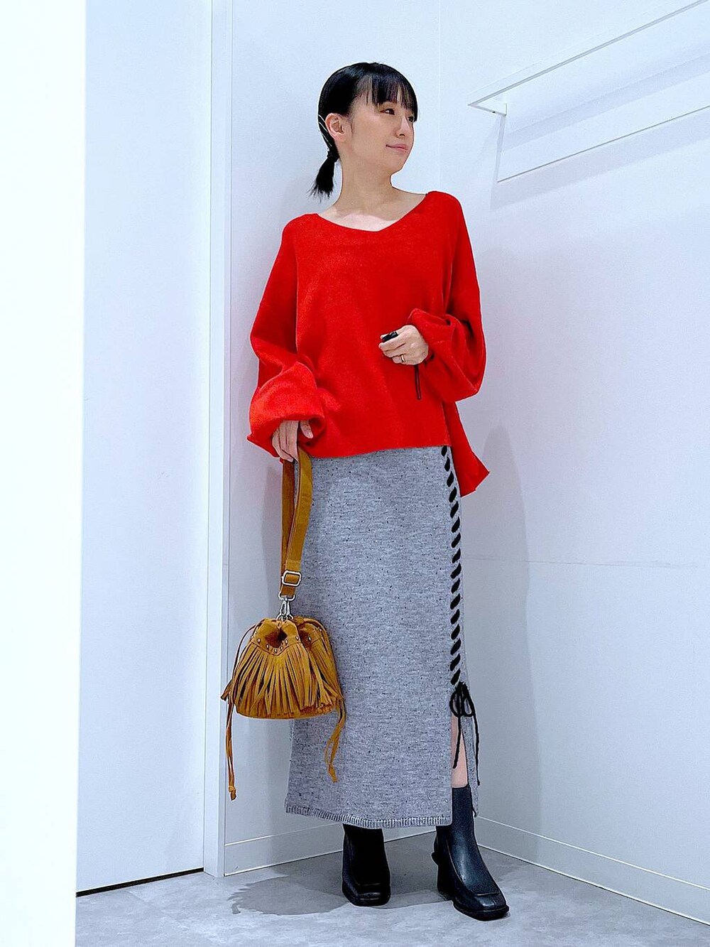レッド系のニット/セーター、グレー系のスカート、ブラック系のブーツを着用したレディースの秋コーディネートの2枚目の写真