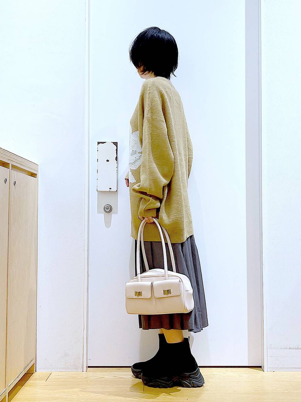 ホワイト系のハンドバッグ、ブラック系のブーツ、グレー系のスカートを着用したレディースの冬コーディネートの3枚目の写真