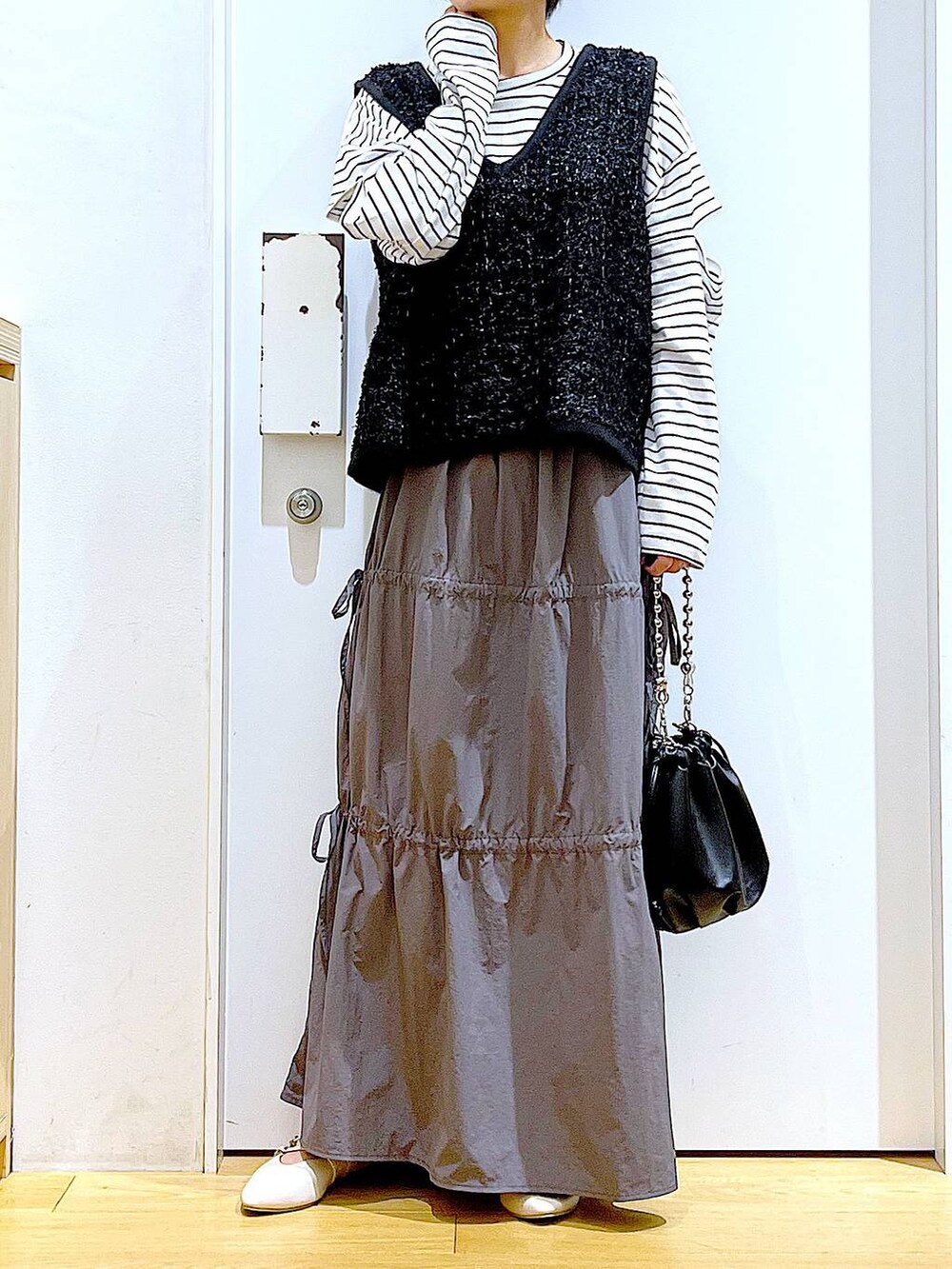 ブラック系のショルダーバッグ、ホワイト系のパンプス、グレー系のスカートを着用したレディースの秋コーディネートの6枚目の写真