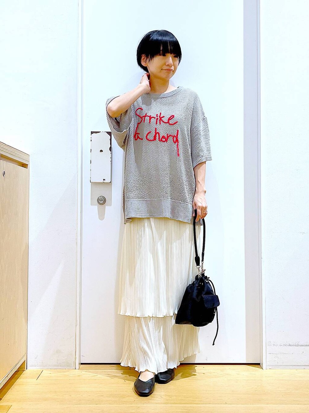 ブラック系のパンプス、ホワイト系のスカート、グレー系のニット/セーターを着用したレディースの春コーディネートの2枚目の写真