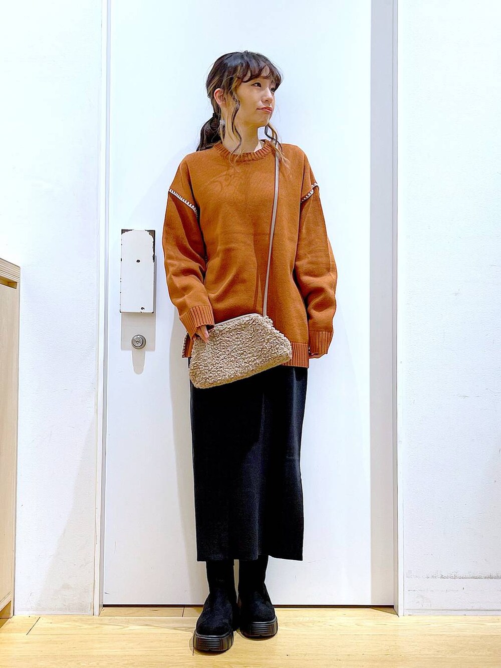 グレー系のスカート、オレンジ系のニット/セーター、ブラウン系のクラッチバッグを着用したレディースの冬コーディネートの2枚目の写真