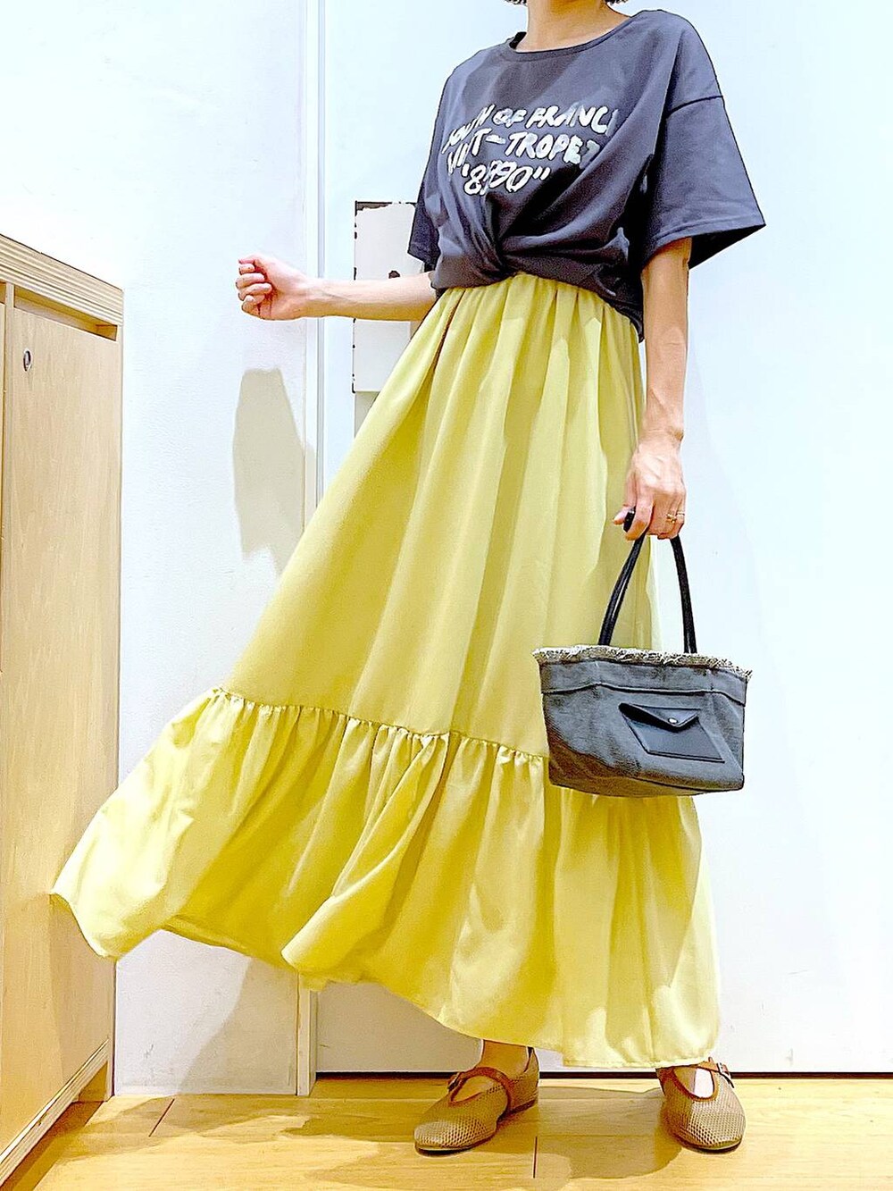 ブラック系のショルダーバッグ、ベージュ系のパンプス、イエロー系のワンピースを着用したレディースの春コーディネートの6枚目の写真