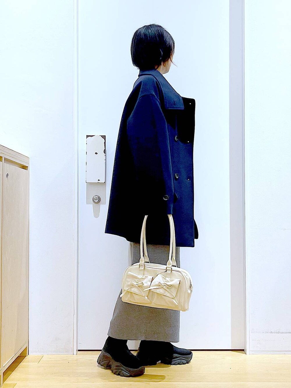 ブルー系のステンカラーコート、ホワイト系のハンドバッグ、ブラック系のブーツを着用したレディースの冬コーディネートの4枚目の写真