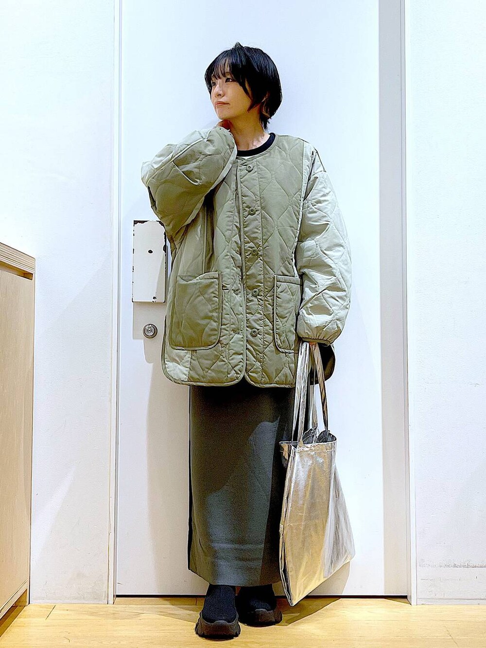 シルバー系のトートバッグ、グレー系のスカート、ブラック系のブーツを着用したレディースの秋コーディネートの2枚目の写真