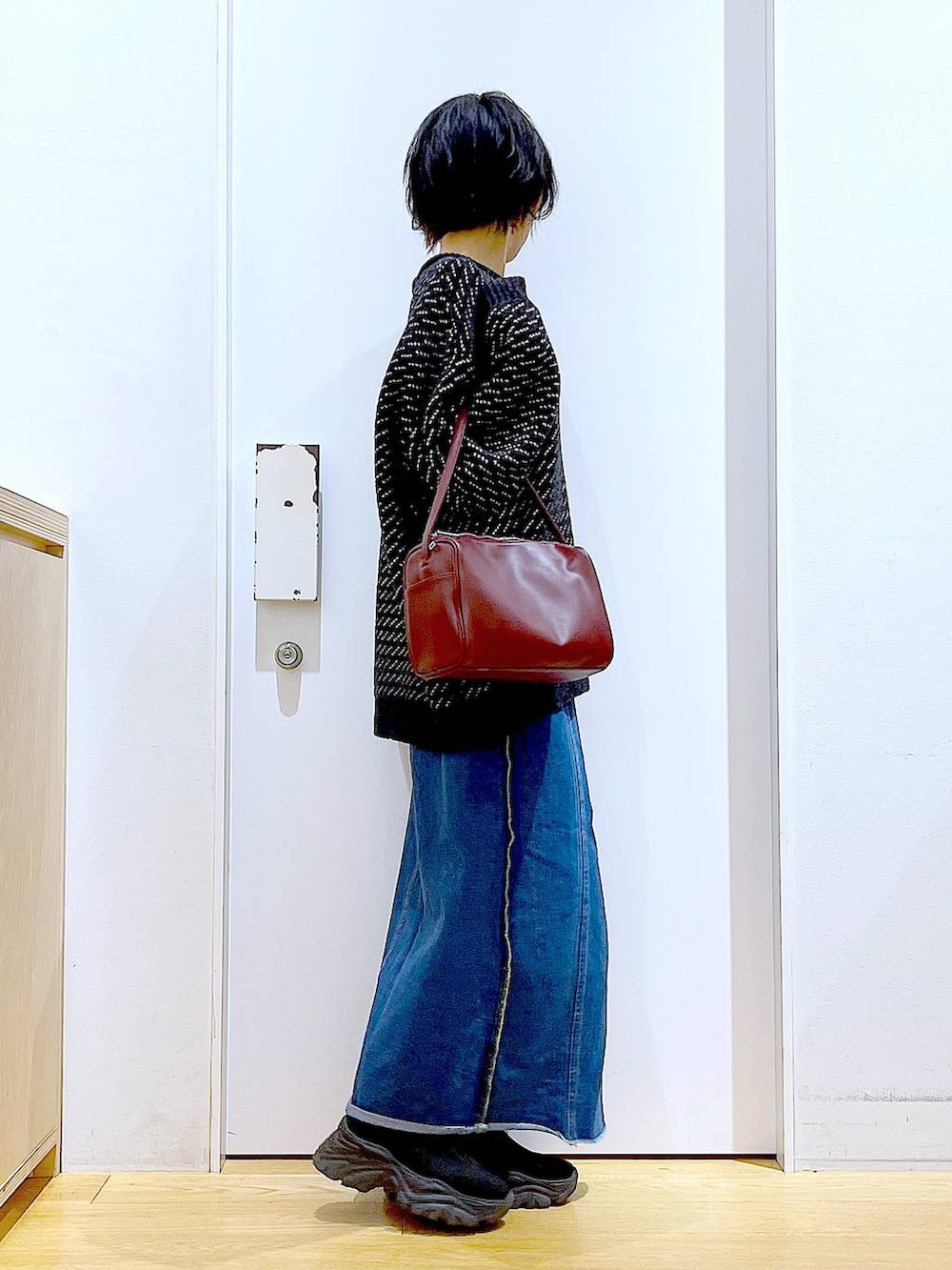 レッド系のショルダーバッグ、ブルー系のデニムスカート、ブラック系のニット/セーターを着用したレディースの冬コーディネートの4枚目の写真