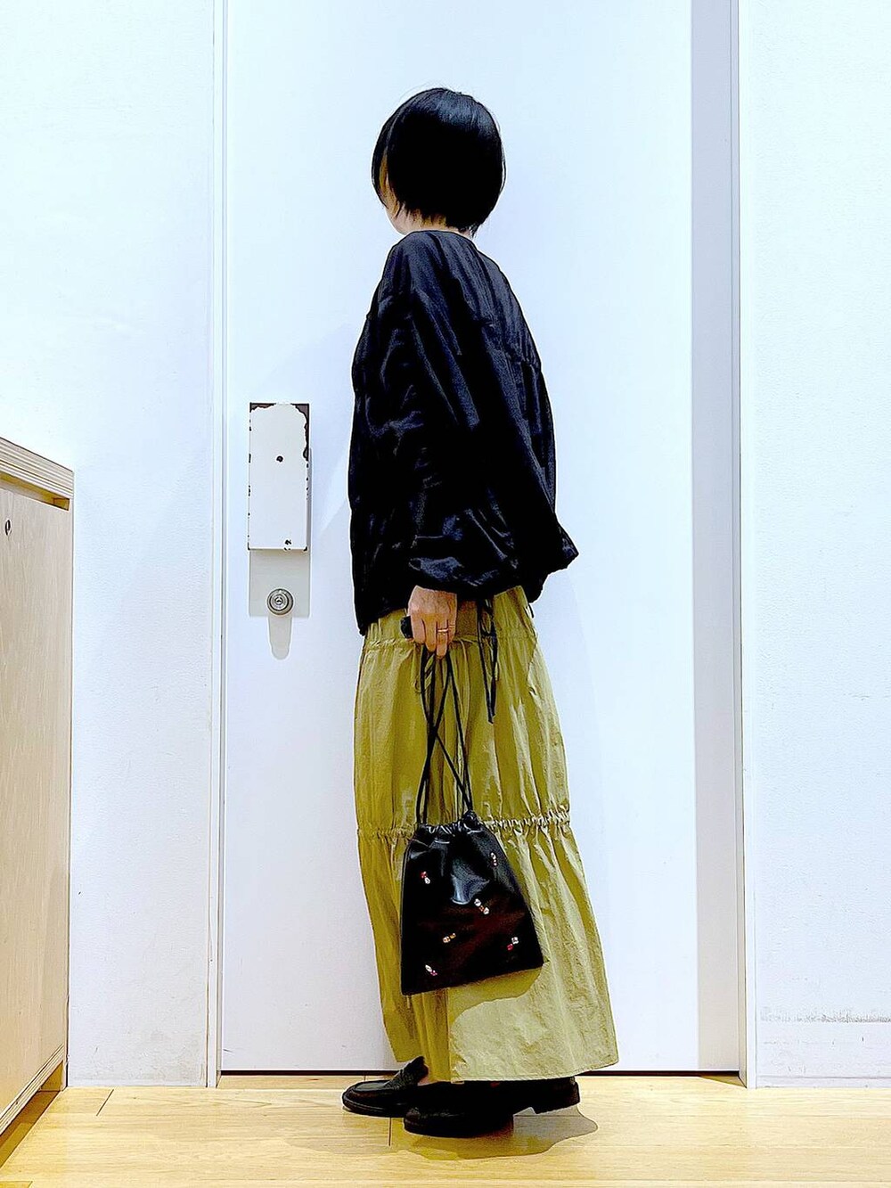 ブラック系のショルダーバッグ、ブラック系のローファー、イエロー系のスカートを着用したレディースの秋コーディネートの3枚目の写真