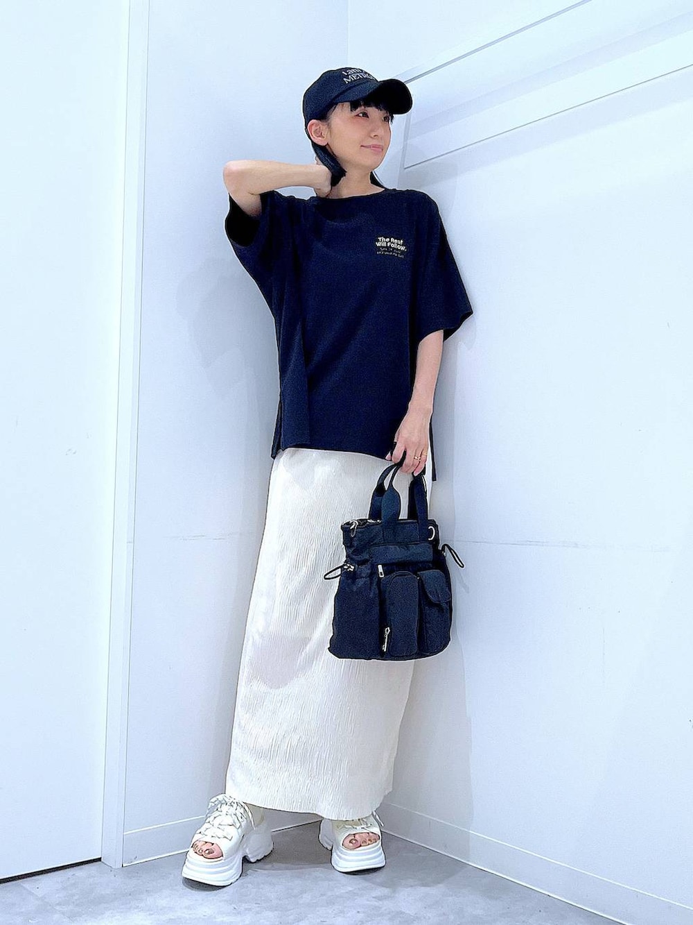 ブラック系のトートバッグ、ホワイト系のサンダル、ブラック系のTシャツ/カットソーを着用したレディースの夏コーディネートの2枚目の写真