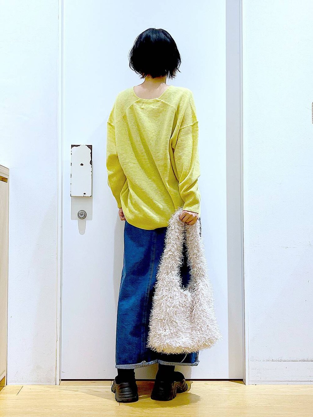 イエロー系のニット/セーター、ブルー系のデニムスカート、ベージュ系のショルダーバッグを着用したレディースの冬コーディネートの5枚目の写真