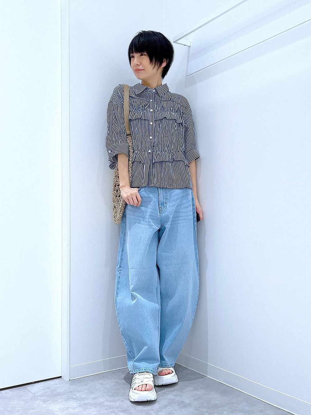 ブルー系のデニムパンツ、ベージュ系のトートバッグ、ホワイト系のスニーカーを着用したレディースの夏コーディネートの2枚目の写真