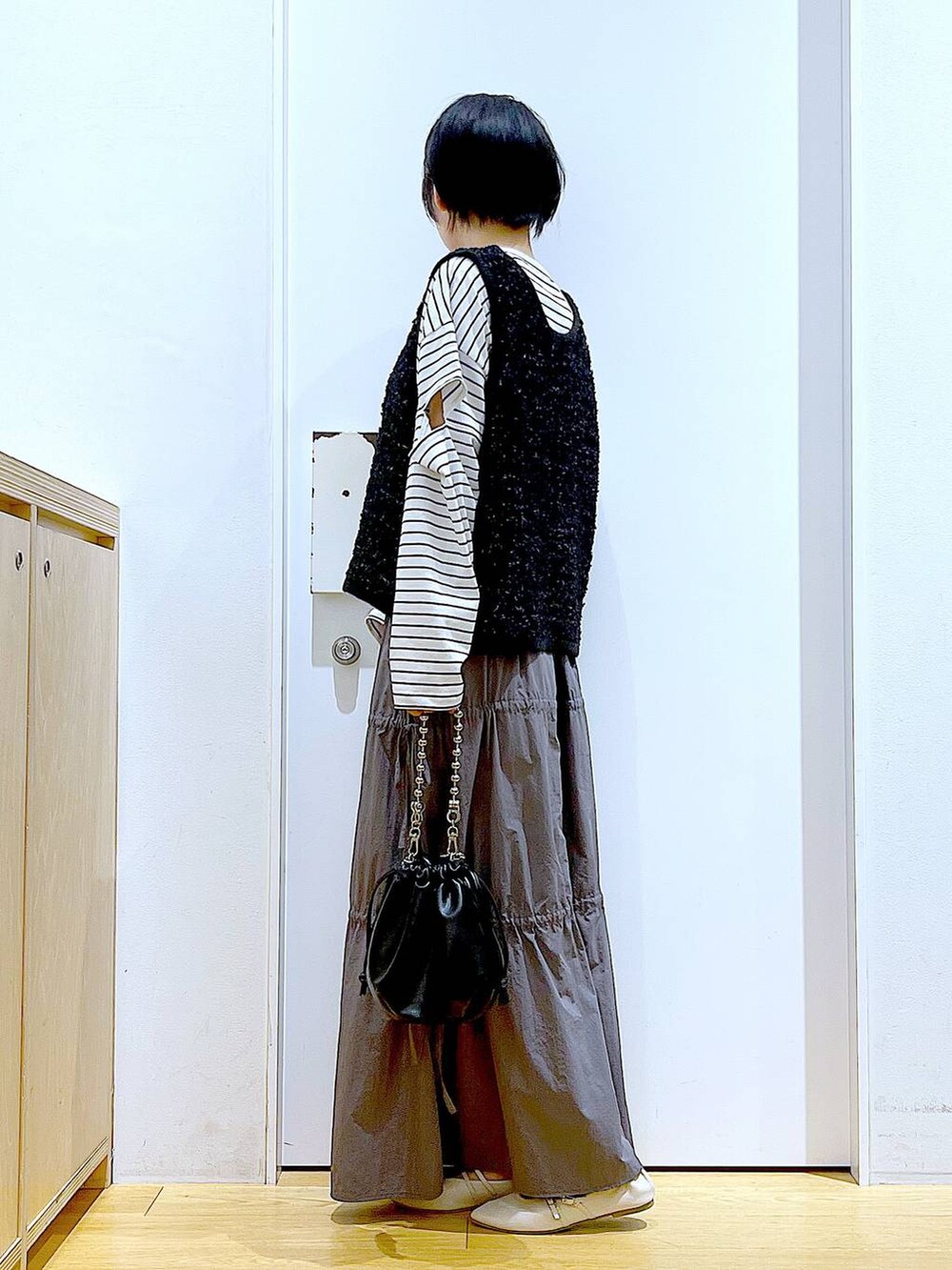 ブラック系のショルダーバッグ、ホワイト系のパンプス、グレー系のスカートを着用したレディースの秋コーディネートの3枚目の写真