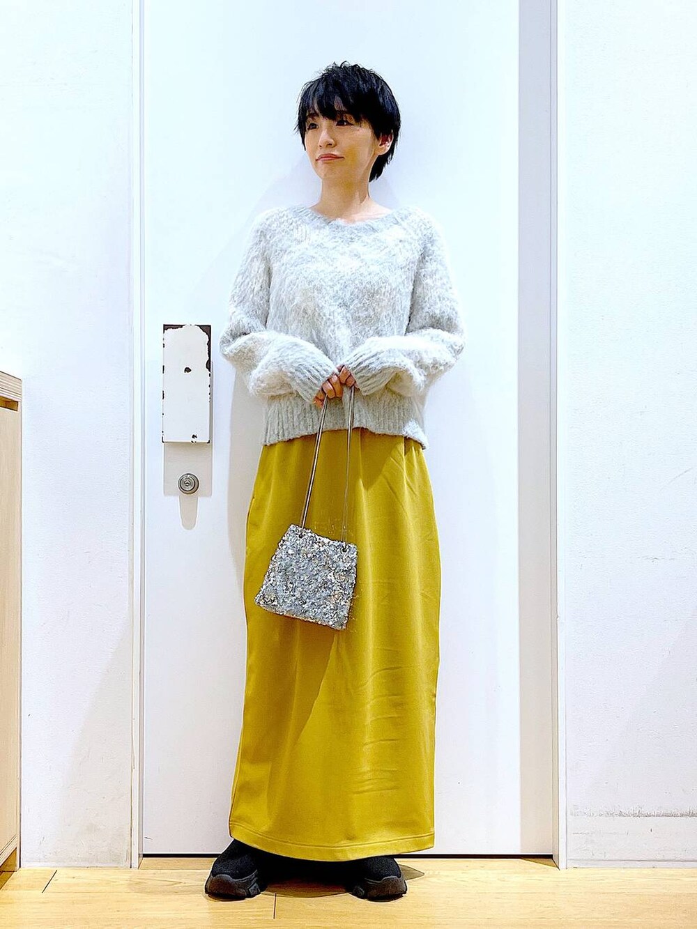 ブラック系のブーツ、イエロー系のスカート、その他のショルダーバッグを着用したレディースの冬コーディネートの2枚目の写真