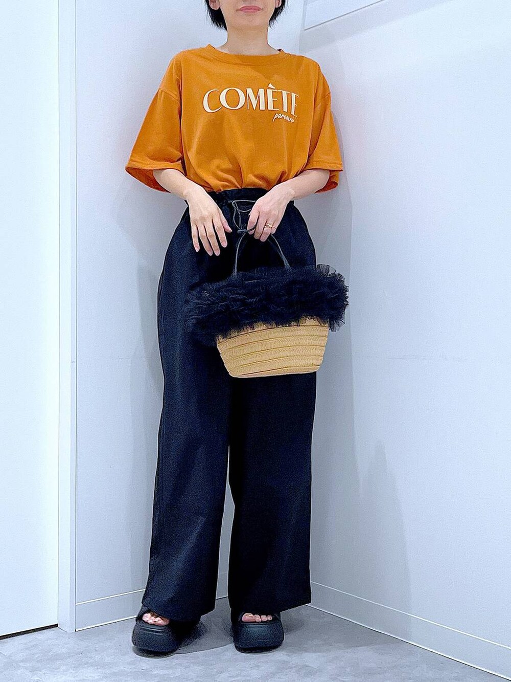 ベージュ系のショルダーバッグ、ブラック系のサンダル、オレンジ系のTシャツ/カットソーを着用したレディースの夏コーディネートの6枚目の写真