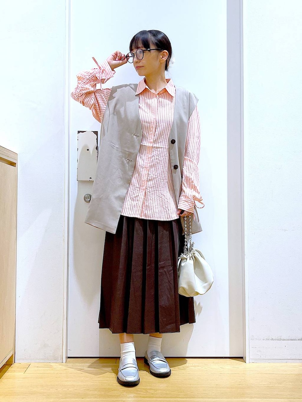 ベージュ系のショルダーバッグ、シルバー系のローファー、ベージュ系のベストを着用したレディースの秋コーディネートの2枚目の写真