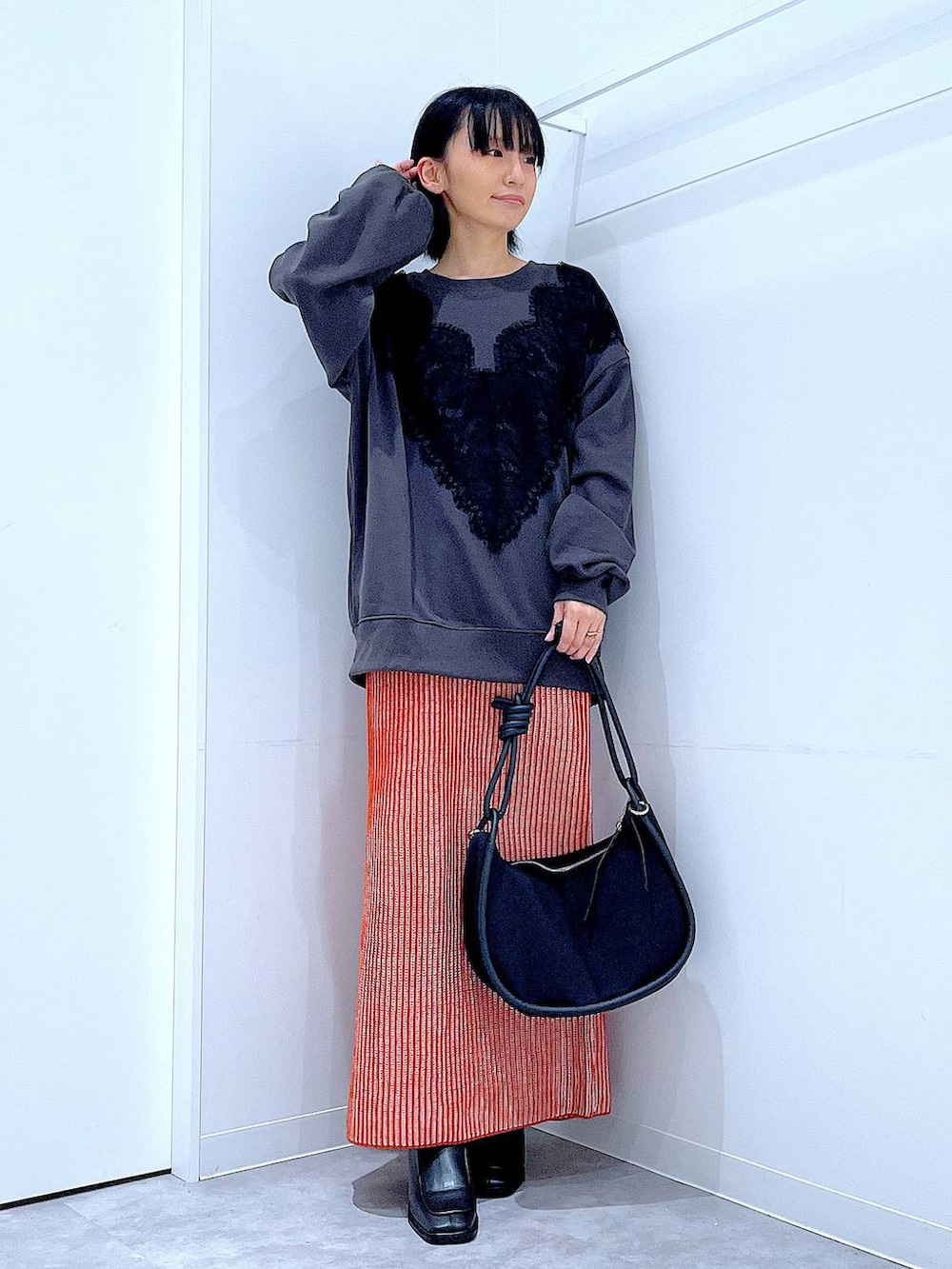 オレンジ系のスカート、ブラック系のブーツ、ブラック系のショルダーバッグを着用したレディースの秋コーディネートの2枚目の写真