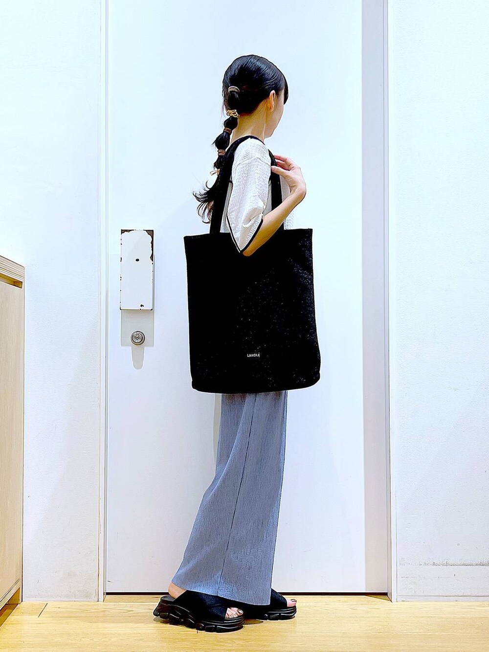 ブラック系のトートバッグ、ブラック系のサンダル、ホワイト系のTシャツ/カットソーを着用したレディースの夏コーディネートの4枚目の写真