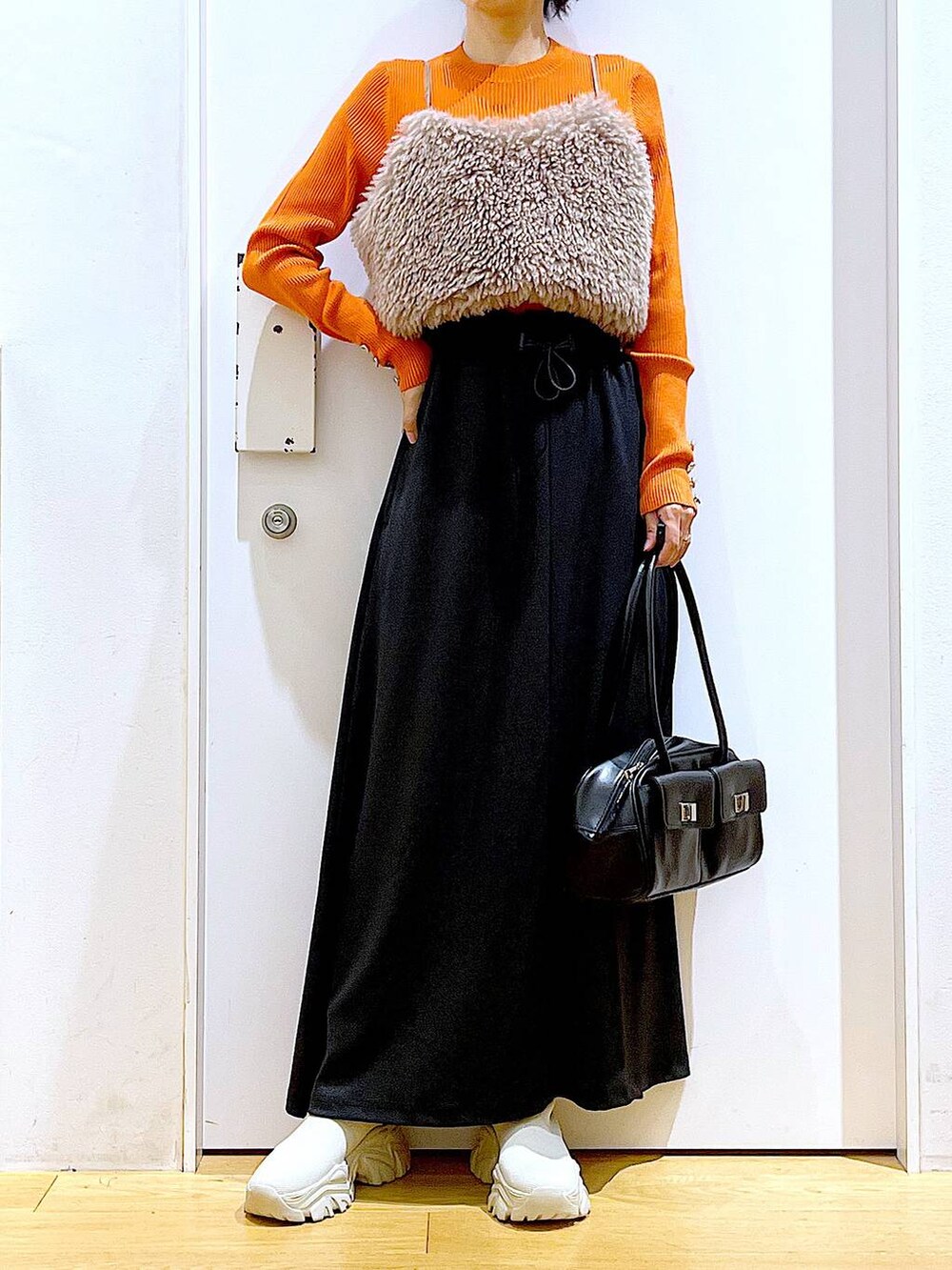 オレンジ系のニット/セーター、ブラウン系のベスト、ブラック系のハンドバッグを着用したレディースの秋コーディネートの6枚目の写真