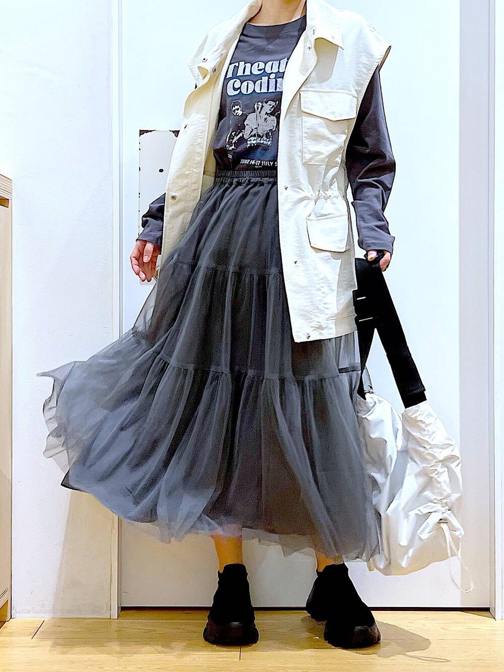 グレー系のスカート、ブラック系のスニーカー、ホワイト系のベストを着用したレディースの春コーディネートの6枚目の写真