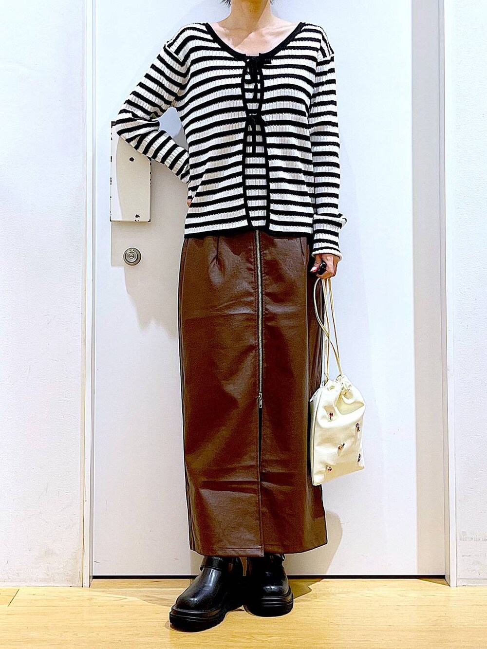 ブラウン系のスカート、ホワイト系のショルダーバッグ、ブラック系のブーツを着用したレディースの秋コーディネートの6枚目の写真