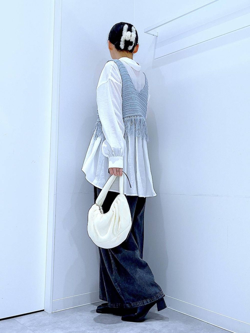 ブラック系のブーツ、ブルー系のベスト、ホワイト系のショルダーバッグを着用したレディースの春コーディネートの3枚目の写真