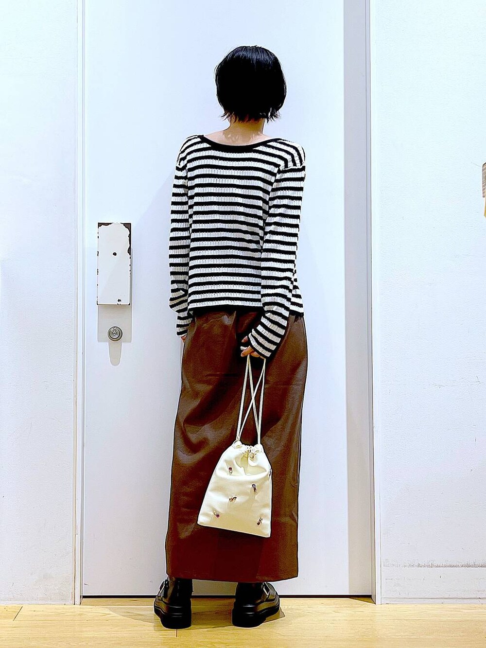 ブラウン系のスカート、ホワイト系のショルダーバッグ、ブラック系のブーツを着用したレディースの秋コーディネートの5枚目の写真