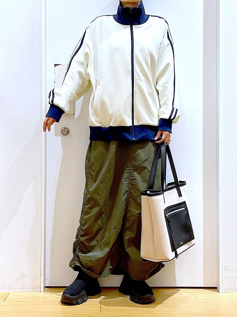 ホワイト系のトートバッグ、ブラック系のブーツ、グリーン系のスカートを着用したレディースの冬コーディネートの6枚目の写真