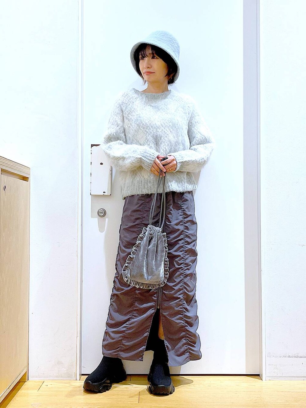 グレー系のショルダーバッグ、グレー系のスカート、ブラック系のブーツを着用したレディースの冬コーディネートの2枚目の写真