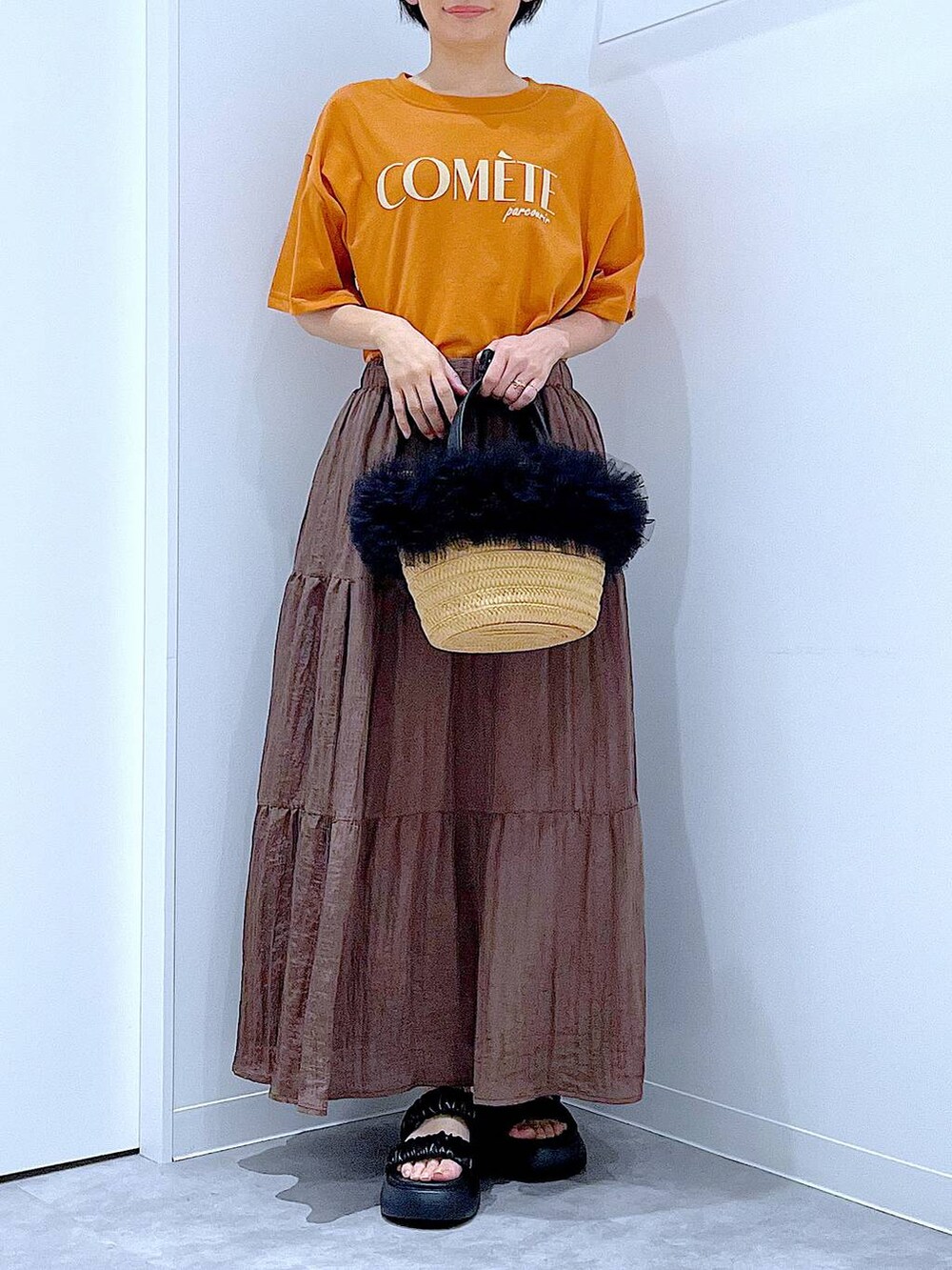 ベージュ系のショルダーバッグ、ブラック系のサンダル、オレンジ系のTシャツ/カットソーを着用したレディースの夏コーディネートの6枚目の写真