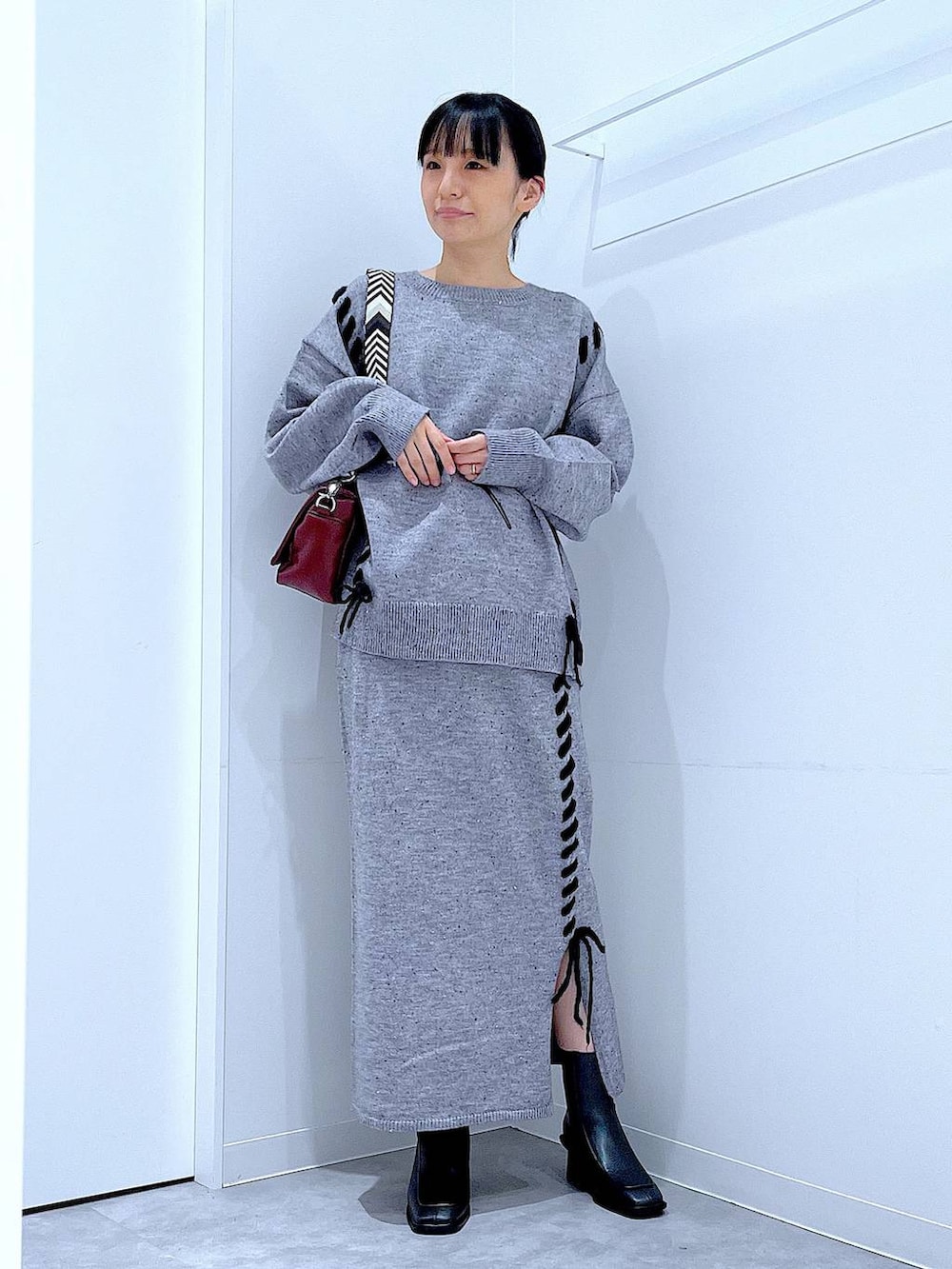 グレー系のニット/セーター、レッド系のショルダーバッグ、グレー系のスカートを着用したレディースの冬コーディネートの2枚目の写真