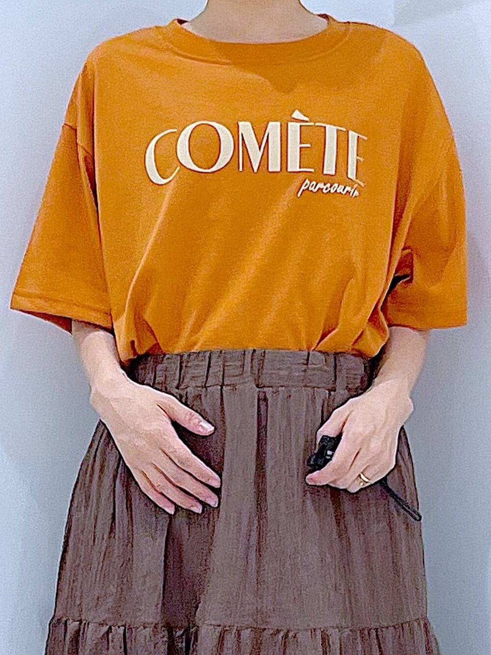 ベージュ系のショルダーバッグ、ブラック系のサンダル、オレンジ系のTシャツ/カットソーを着用したレディースの夏コーディネートの7枚目の写真