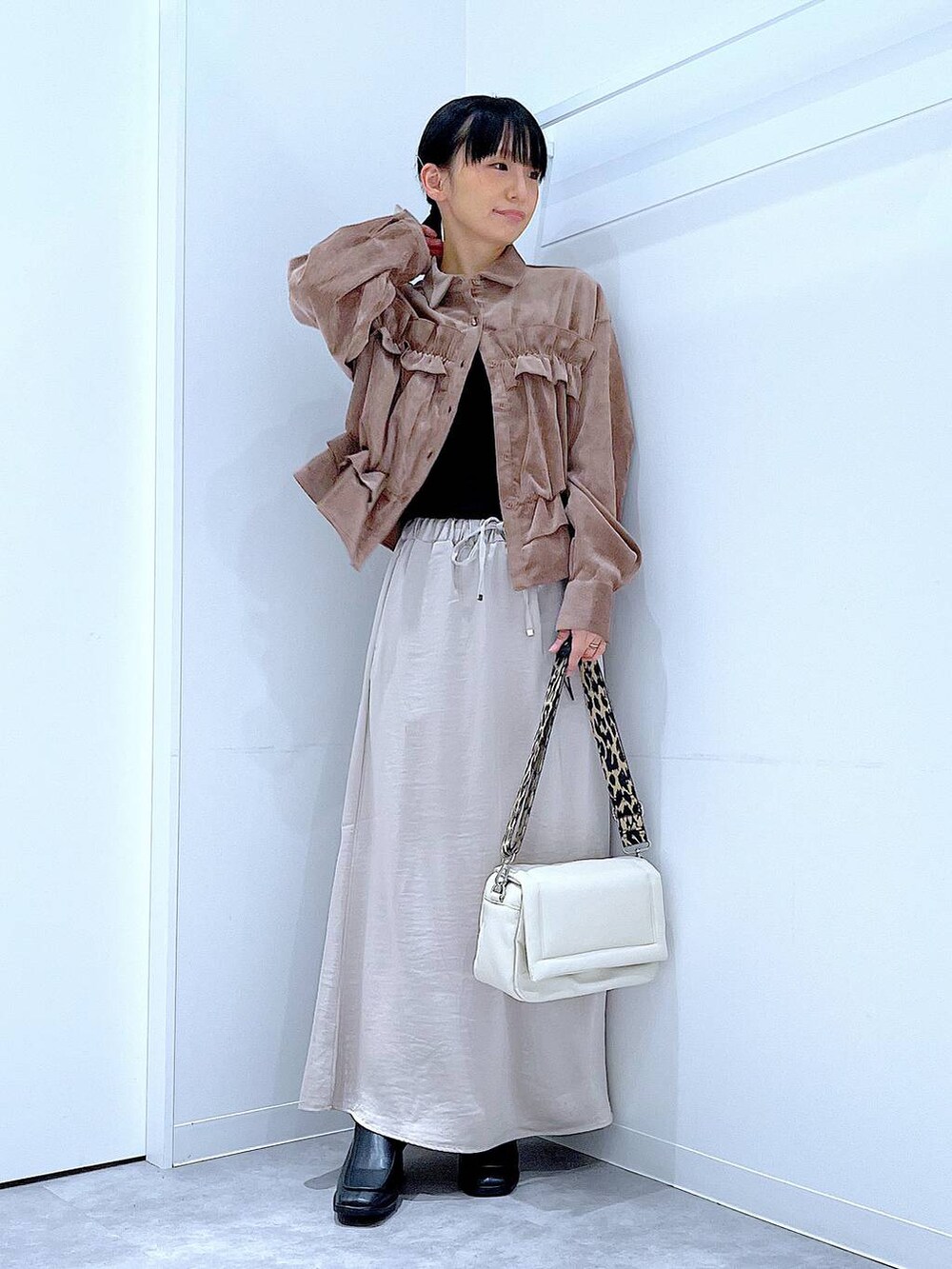 ベージュ系のスカート、ホワイト系のショルダーバッグ、ブラック系のブーツを着用したレディースの秋コーディネートの2枚目の写真