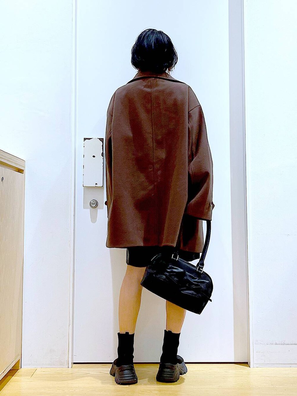 ブラウン系のステンカラーコート、ブラック系のハンドバッグ、ブラック系のブーツを着用したレディースの冬コーディネートの5枚目の写真