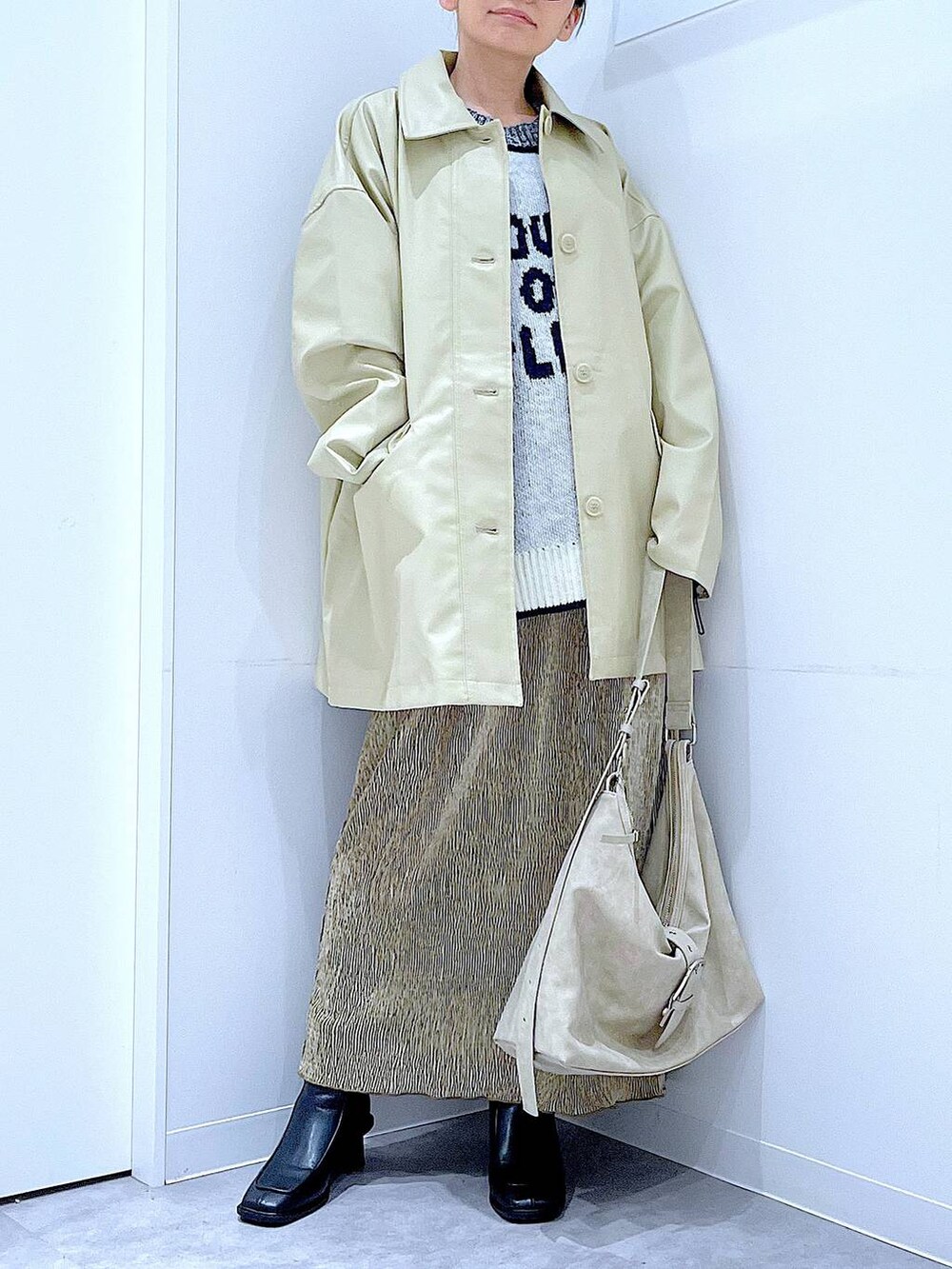 ベージュ系のステンカラーコート、ブラック系のブーツ、ホワイト系のショルダーバッグを着用したレディースの冬コーディネートの6枚目の写真