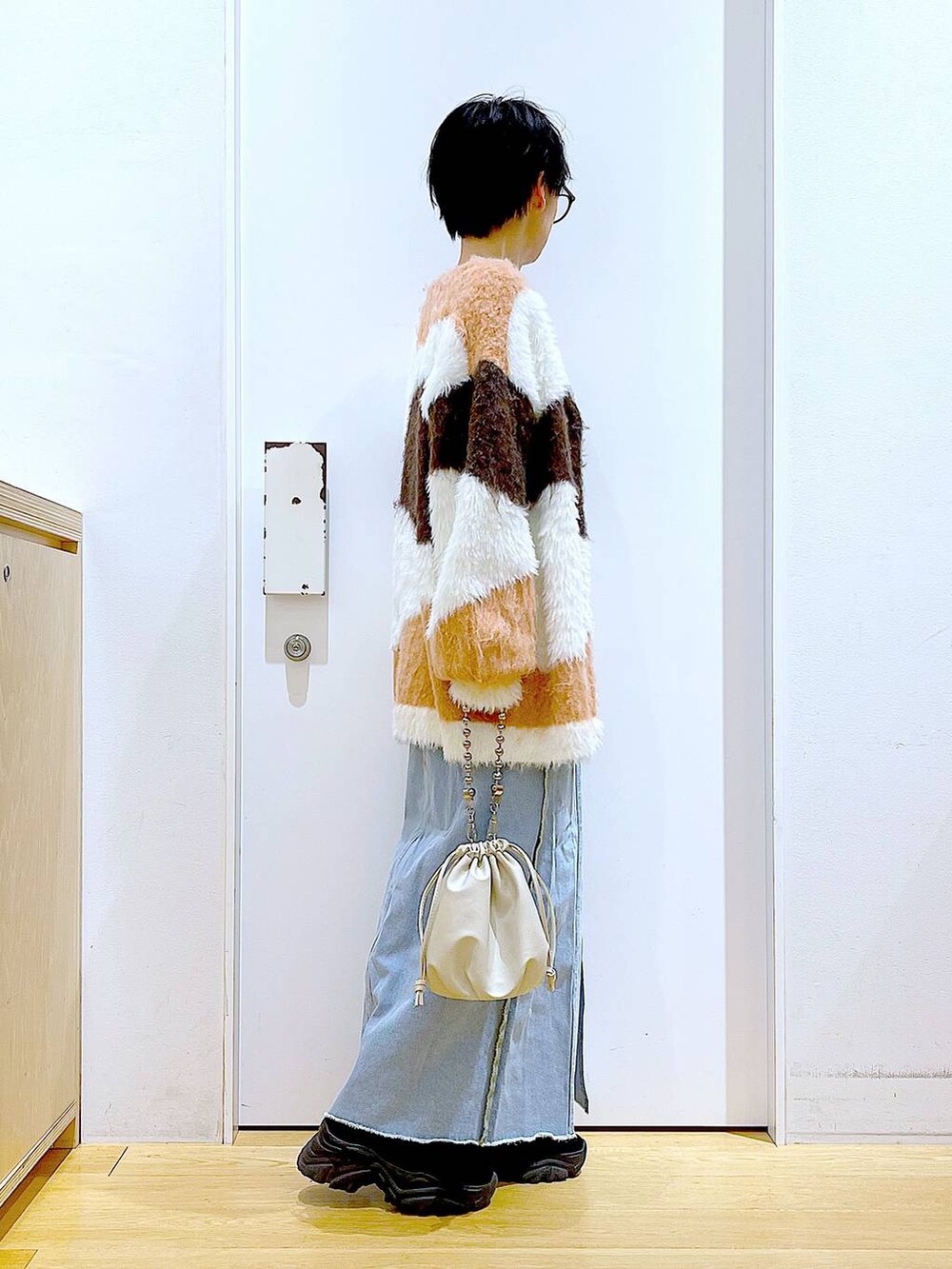 ベージュ系のショルダーバッグ、ブルー系のデニムスカート、ブラック系のブーツを着用したレディースの冬コーディネートの4枚目の写真