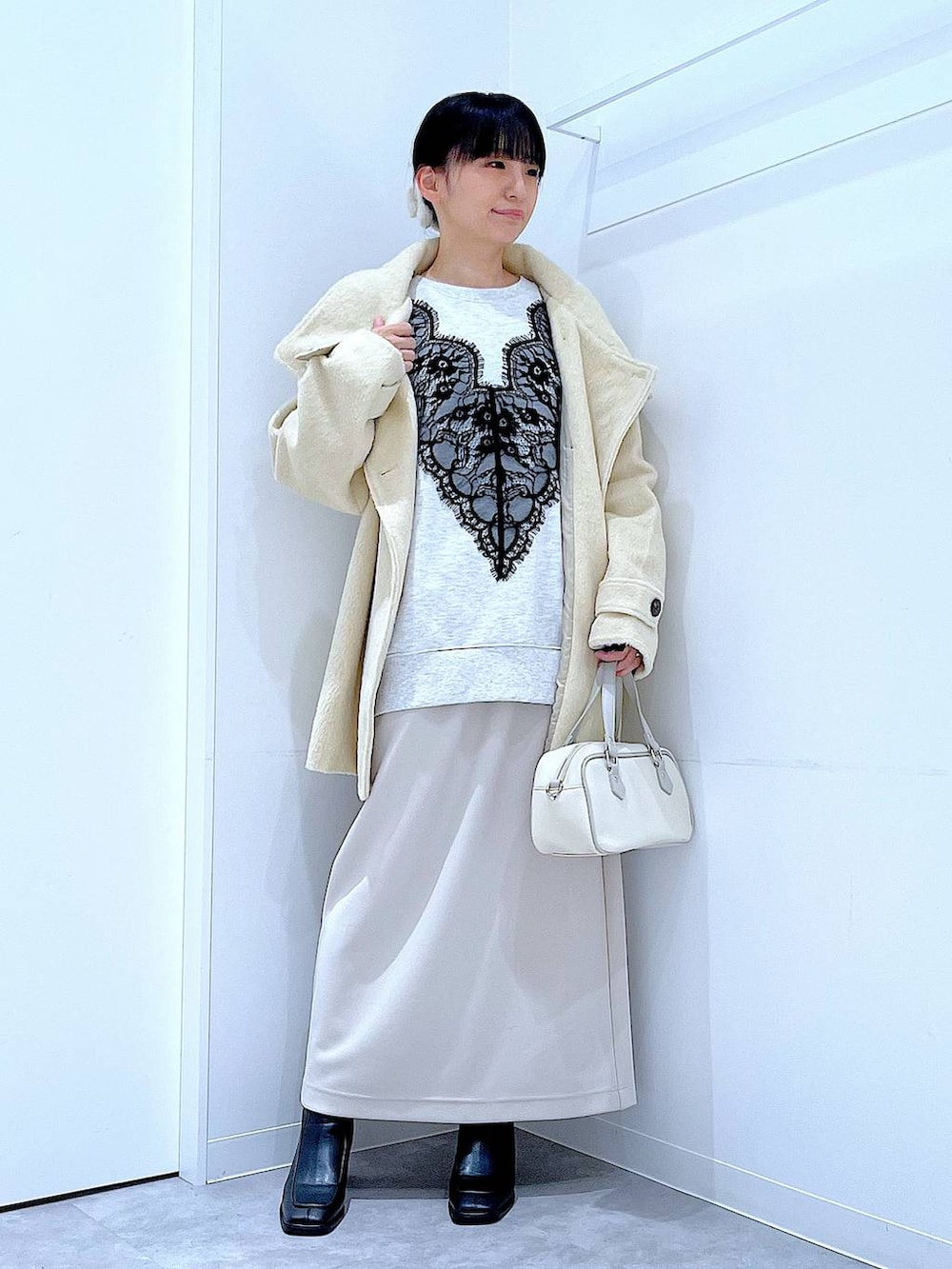 ベージュ系のスカート、ベージュ系のステンカラーコート、ブラック系のブーツを着用したレディースの冬コーディネートの2枚目の写真