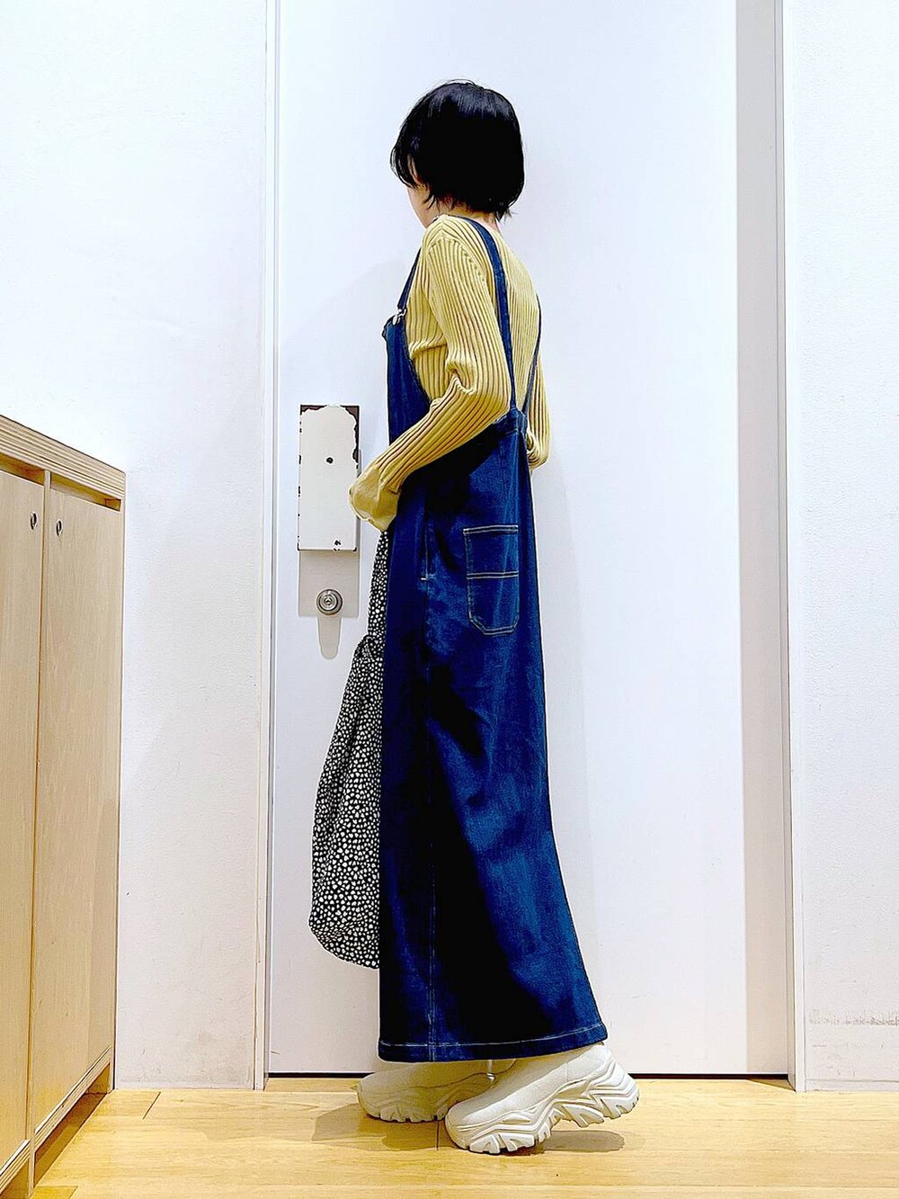 ブルー系のジャンパースカート、ブラック系のトートバッグ、イエロー系のニット/セーターを着用したレディースの秋コーディネートの3枚目の写真