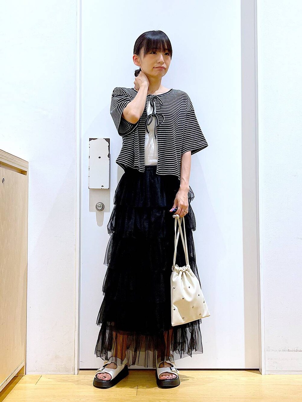 ホワイト系のサンダル、ホワイト系のショルダーバッグ、ブラック系のスカートを着用したレディースの夏コーディネートの2枚目の写真