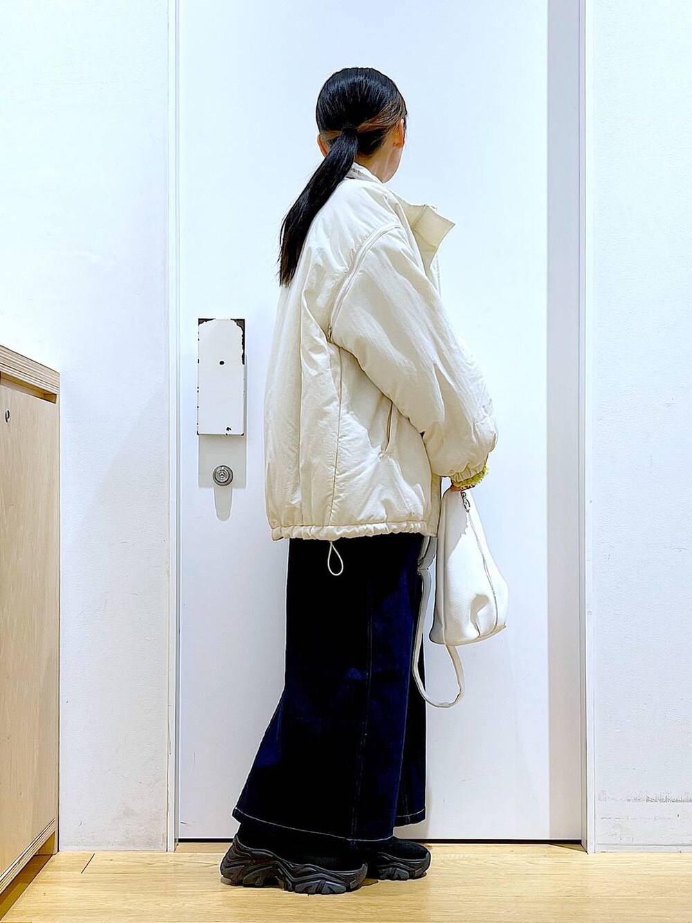 グリーン系のニット/セーター、ブルー系のジャンパースカート、ホワイト系のボディバッグ/ウエストポーチを着用したレディースの冬コーディネートの4枚目の写真