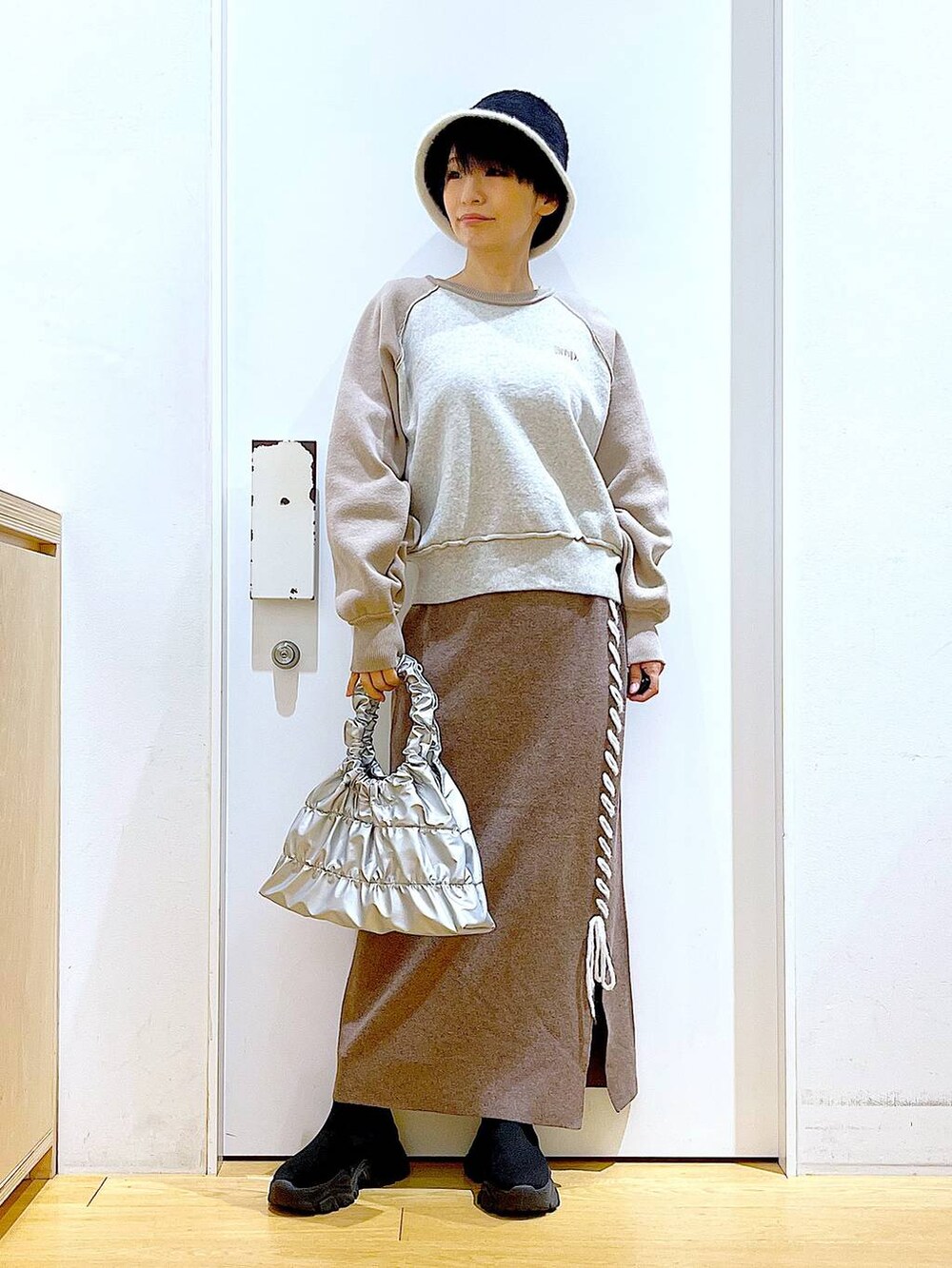 ブラック系のブーツ、ブラウン系のスカート、シルバー系のショルダーバッグを着用したレディースの冬コーディネートの2枚目の写真