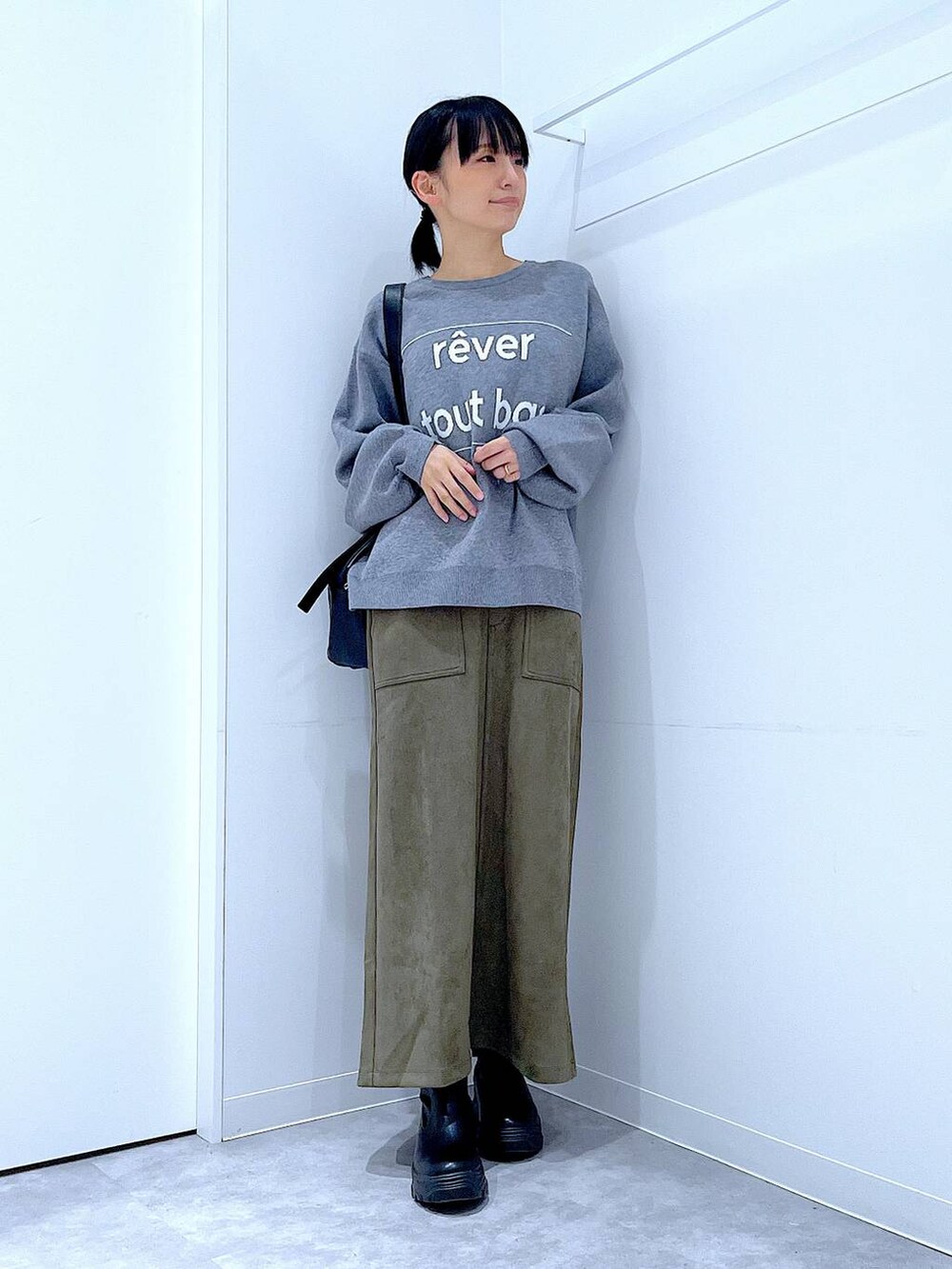 ブラック系のショルダーバッグ、ブラック系のブーツ、グリーン系のスカートを着用したレディースの冬コーディネートの2枚目の写真