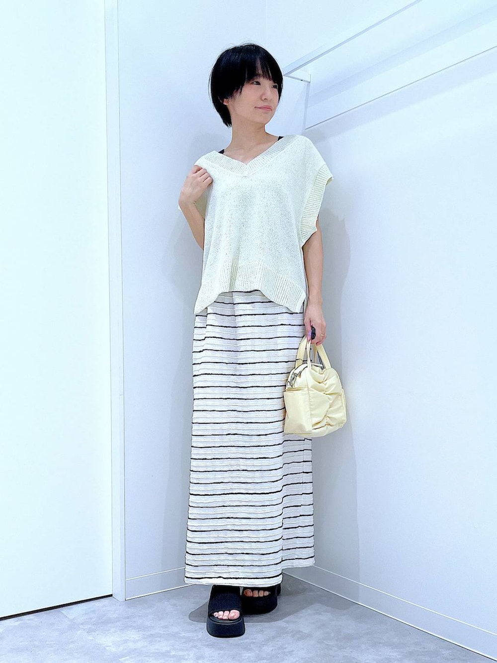 ブラック系のサンダル、イエロー系のショルダーバッグ、ホワイト系のスカートを着用したレディースの夏コーディネートの2枚目の写真