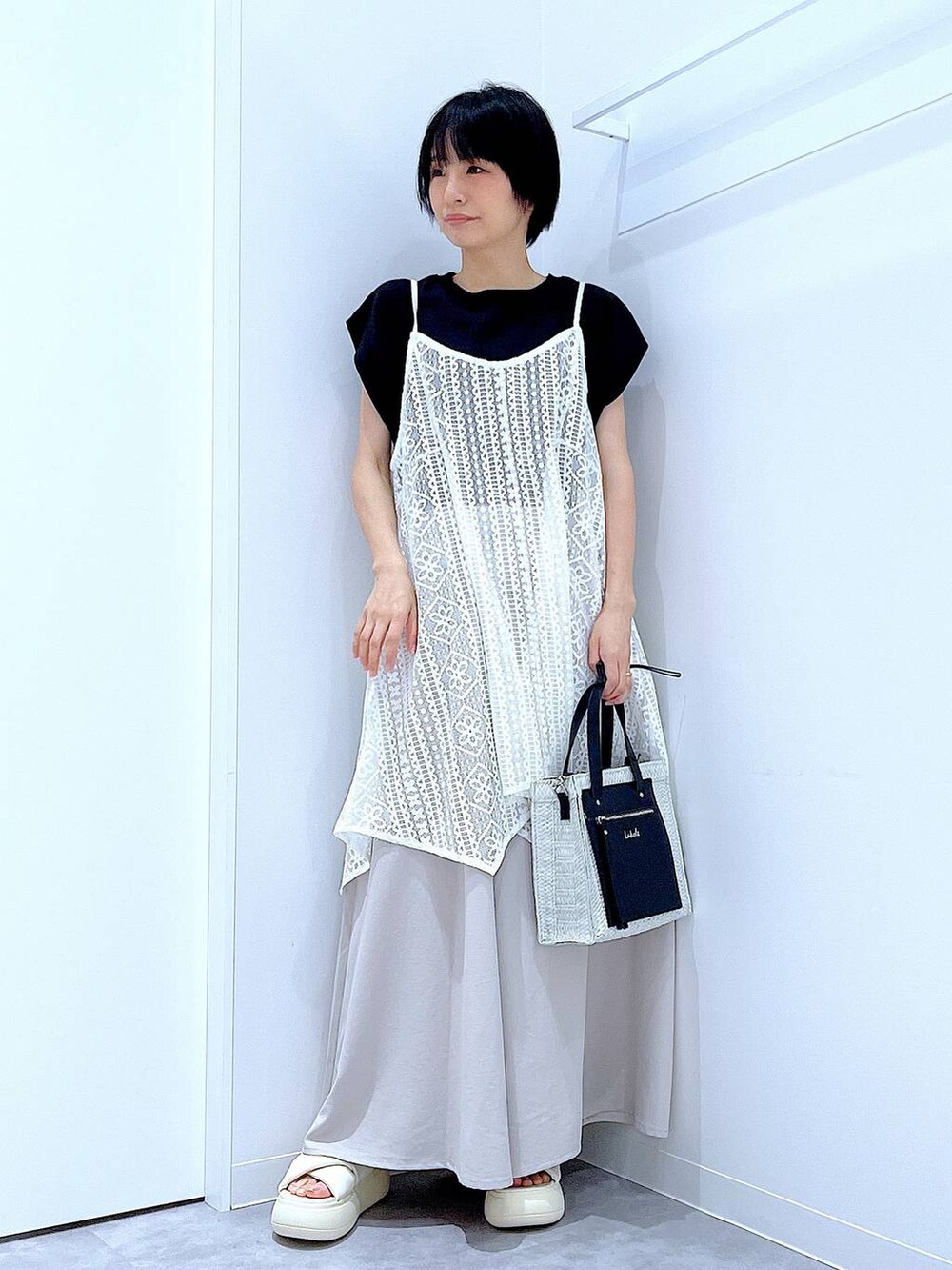 ホワイト系のショルダーバッグ、ホワイト系のサンダル、ブラック系のTシャツ/カットソーを着用したレディースの夏コーディネートの2枚目の写真