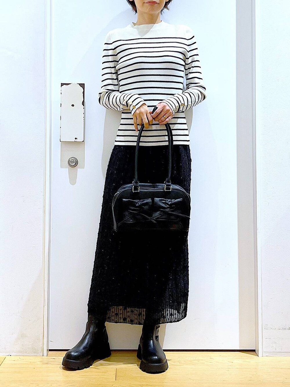 ホワイト系のニット/セーター、ブラック系のハンドバッグ、ブラック系のブーツを着用したレディースの秋コーディネートの6枚目の写真