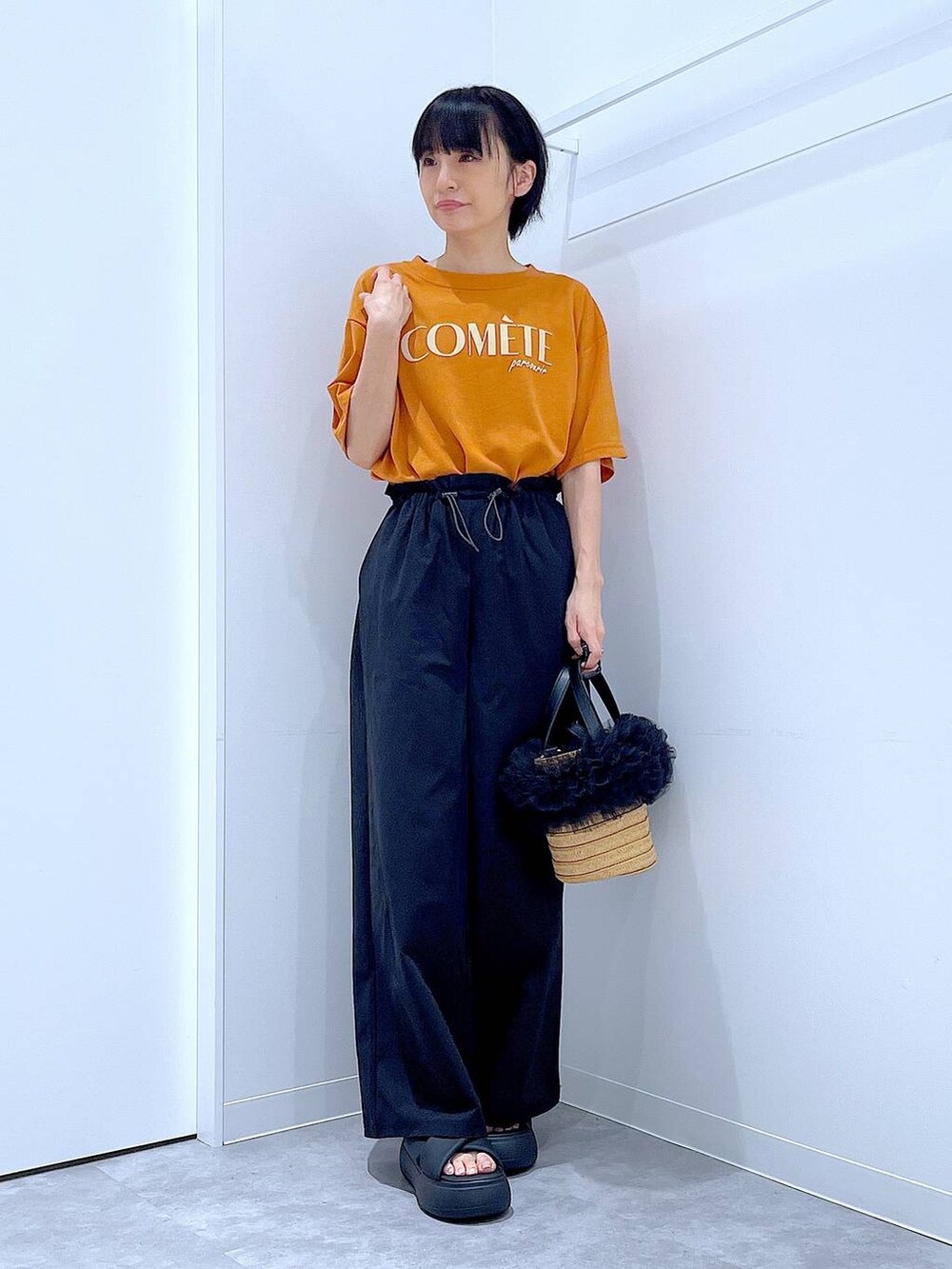 ベージュ系のショルダーバッグ、ブラック系のサンダル、オレンジ系のTシャツ/カットソーを着用したレディースの夏コーディネートの2枚目の写真