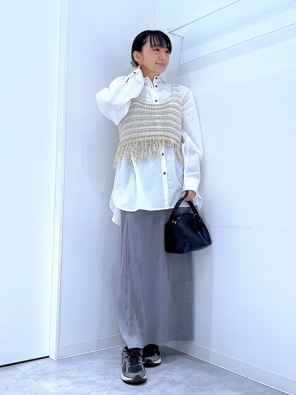 ブラック系のショルダーバッグ、ベージュ系のベスト、グレー系のスカートを着用したレディースの春コーディネートの2枚目の写真